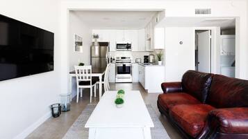 A modern living room with a white coffee table, a red leather sofa, and a dining area with white chairs.