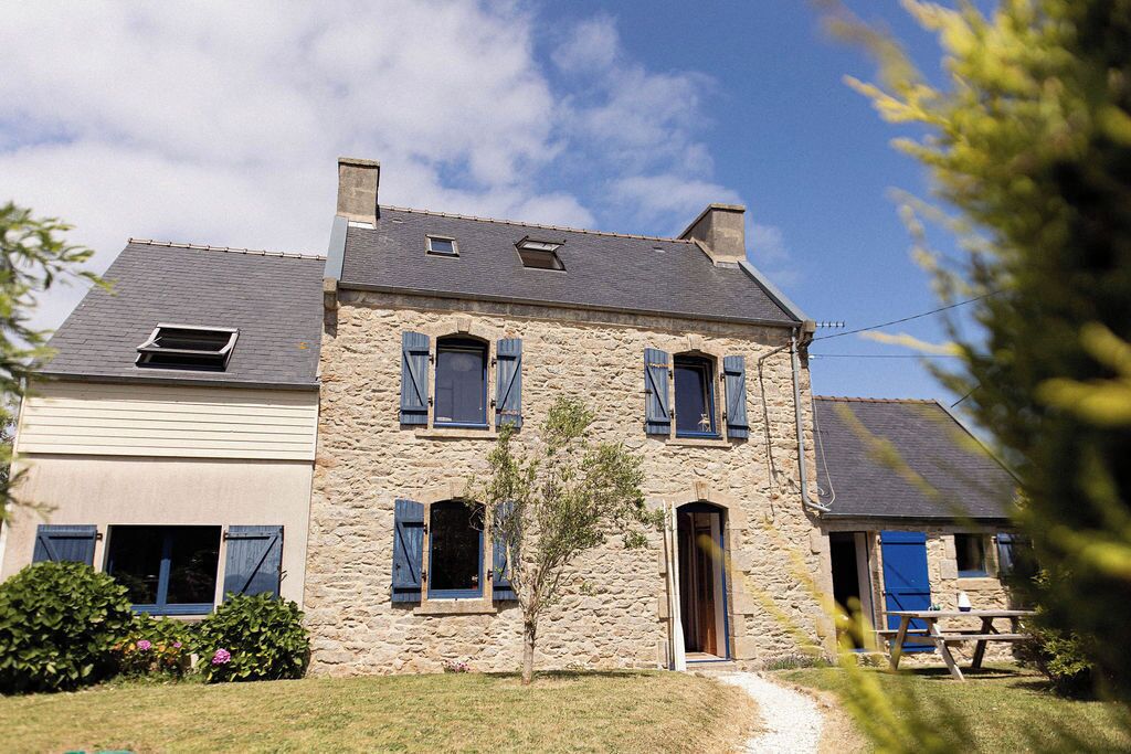 A stone house with a sloped roof, multiple windows with shutters, and a visible door.