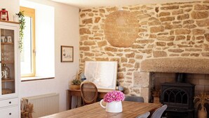 A cozy dining area with a stone wall, a fireplace, and a wooden table with chairs. - Ty Glaz Lilia (Plouguerneau)