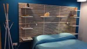 Una camera da letto con un letto, un comodino, una lampada e una mensola a parete con oggetti decorativi.