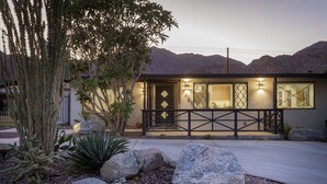 A modern house with a large front porch, a well-maintained garden with rocks and cacti, and a mountain backdrop. - Travel Back in Time to this Gorgeous 1950's Remodel (La Quinta,)