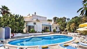 A pool area with lounge chairs and a building with a tiled roof.