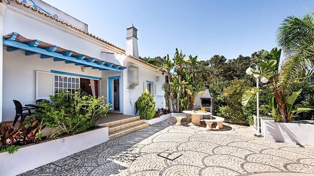 A courtyard with a tiled floor, a pool, and a building with a blue awning and white walls.