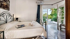 A bedroom with a bed, a bedside table, an air conditioning unit, and a view of the outdoors.