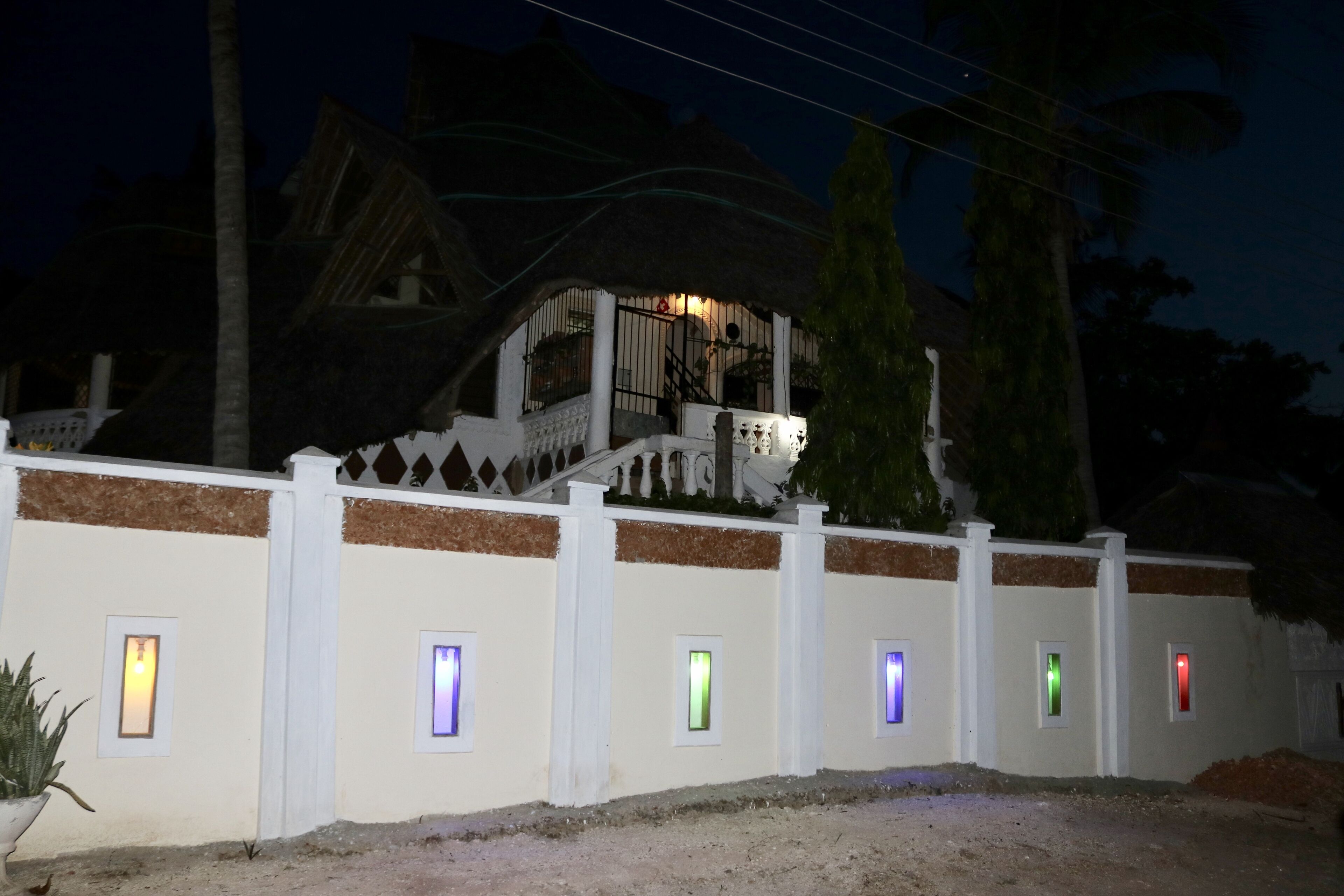 Un edificio con fachada blanca y techo de paja. Se observan varias ventanas pequeñas con luces de colores.