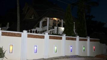 Un edificio con fachada blanca y techo de paja. Se observan varias ventanas pequeñas con luces de colores.