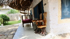 Un espace extérieur aménagé dans un style rustique, avec un banc en bois et une chaise, un toit de chaume et un mur extérieur peint en blanc.