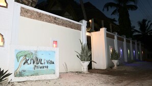 Une entrée privée menant à la villa, avec un panneau indicateur, un pot de fleurs et un chemin qui mène au bâtiment.