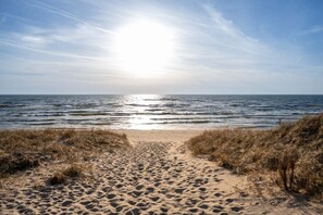 Un sentier de sable qui longe la plage et mène à l’océan, sous un ciel dégagé.