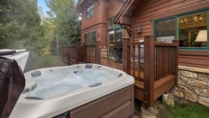 Een hottub buiten een houten chalet met een stenen fundering, omringd door een houten terras en een stenen muur.