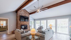 Un salon moderne avec une cheminée en briques, deux canapés, une table basse en verre et un ventilateur de plafond.
