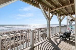 Une terrasse en bois avec une balustrade blanche donnant sur une plage bordée de dunes.