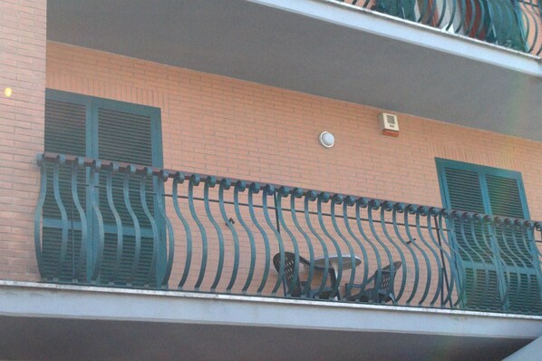 A balcony with a metal railing, a brick wall, and two windows with shutters.