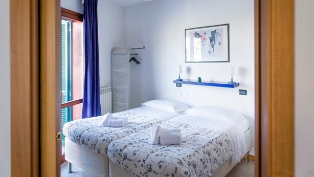 Ein Schlafzimmer mit einem Bett, einem Hängehandtuchhalter, einem an der Wand befestigten Regal mit zwei Lampen und einem Fenster mit blauen Vorhängen.