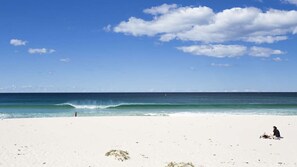 En strand med vit sand, klarblå himmel och vågor som rullar in mot land.