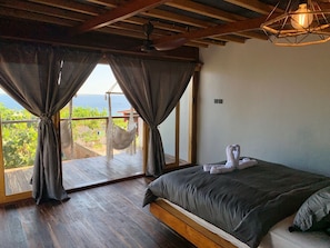 A bedroom with a large bed, wooden floor, and a view of the sea through a balcony. - Restaurant and Villas (Bira)