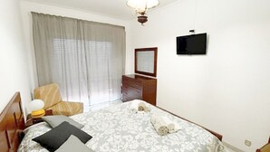 Un dormitorio con una cama, un televisor en la pared, un aparador y una silla.