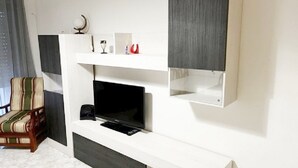 Una sala moderna con un televisor de pantalla plana, una silla de madera y un aparador blanco.