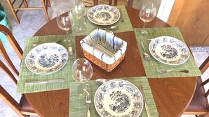 Una mesa de madera redonda con cuatro platos, dos copas de vino y una cesta tejida en el centro.
