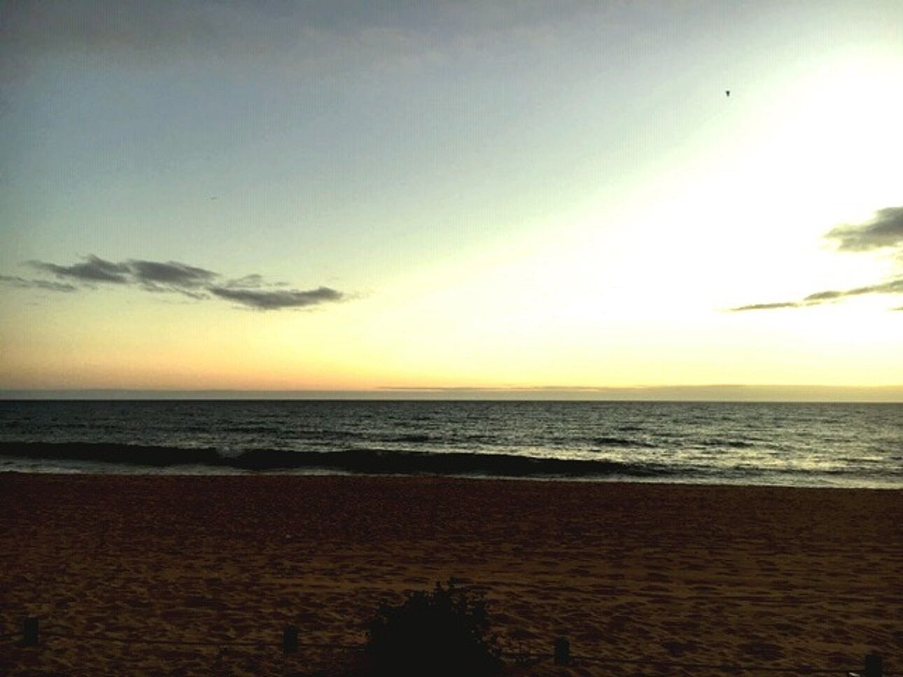 Ein Strand mit freiem Blick auf den Ozean und einem Sonnenuntergang im Hintergrund.