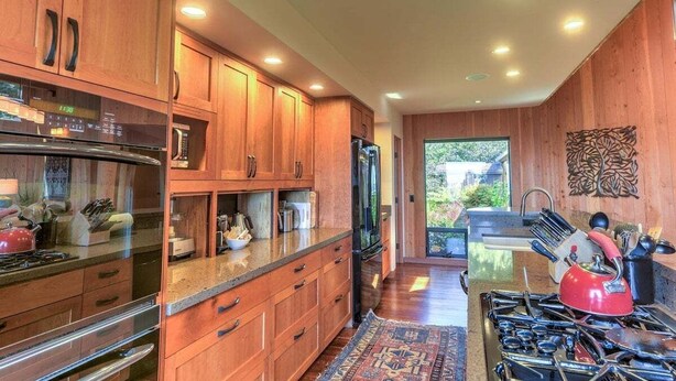 A modern kitchen with wooden cabinets, stainless steel appliances, and a view to the outside. - Redwood | Japanese-Inspired Retreat by the Sea (Sea Ranch)