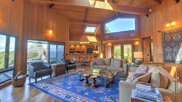 A spacious living area with wooden walls, a large window, and a dining area with a table and chairs. - Redwood | Japanese-Inspired Retreat by the Sea (Sea Ranch)