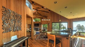 A spacious interior with a piano, a dining area, and a kitchen with a large window. - Redwood | Japanese-Inspired Retreat by the Sea (Sea Ranch)