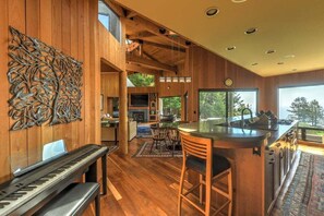 A spacious interior with a piano, a dining area, and a kitchen with a large window. - Redwood | Japanese-Inspired Retreat by the Sea (Sea Ranch)