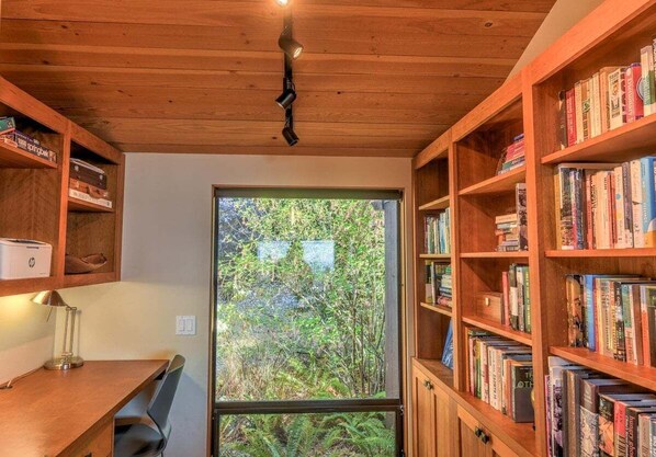 Une pièce avec un bureau en bois, des étagères et une grande fenêtre donnant sur un paysage verdoyant.