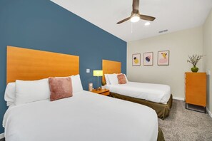Une chambre d’hôtel avec deux lits, un ventilateur de plafond, une table de chevet avec une lampe et des œuvres d’art accrochées au mur.