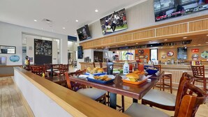 Un restaurant amb un taulell llarg, cadires de fusta i una pantalla de televisió que mostra esports.