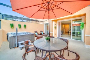 Une terrasse extérieure avec une table en verre, des chaises en osier, un jacuzzi et un parasol.