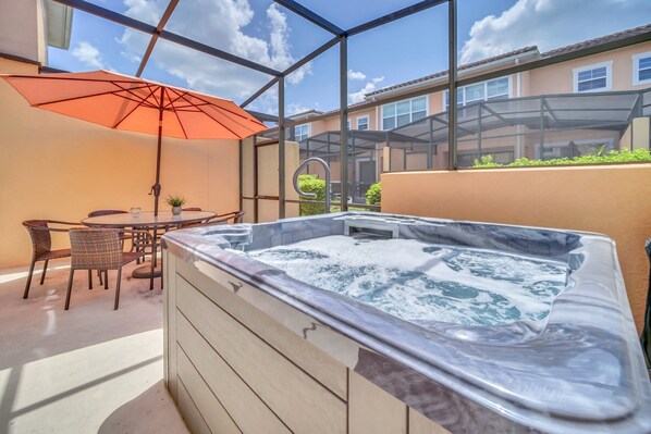 Un bain à remous entouré de parois en verre, une table avec des chaises et un parasol.