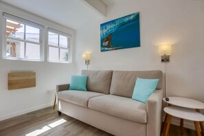 En stue med en beige sofa, to lyseblå puder, et billede af en hval og et lille bord med en fjernbetjening.