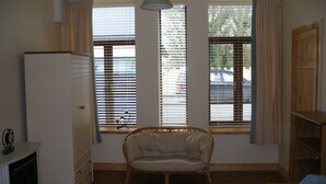 A room with a wooden floor, a wicker chair, a white cabinet, and a window with blinds. - Cooraclare apartment (Cooraclare)