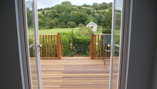A wooden deck with a view of a green landscape and a small white building. - Cooraclare apartment (Cooraclare)