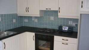 A kitchen with white cabinets, a black countertop, and a blue tiled backsplash. - Cooraclare apartment (Cooraclare)