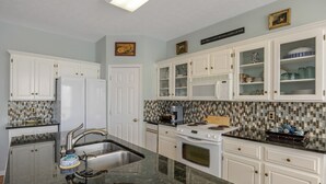 Una cocina con armarios blancos, encimera de granito, pileta de acero inoxidable, estufa y microondas.