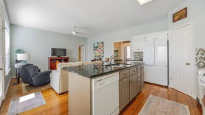 Una cocina compacta con lavavajillas, una zona de comedor con sofá y televisor, y una pequeña isla con lavamanos.