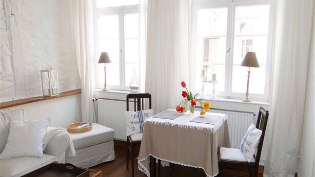 A bright, well-lit room with a white sofa, a small table with a vase of flowers, and a wooden chest. - "Strandläufer" Vacation Rental in Kappeln (Kappeln)