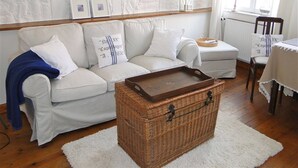A living room with a white sofa, a wicker chest, and a white rug. - "Strandläufer" Vacation Rental in Kappeln (Kappeln)