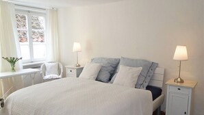 A bedroom with a large bed, two bedside tables with lamps, a chair, and a window with curtains. - "Strandläufer" Vacation Rental in Kappeln (Kappeln)