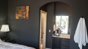 Une chambre à coucher avec un lit, une table de chevet, une lampe, une machine à café et une serviette accrochée au mur.