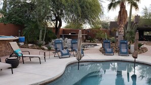Un espace piscine aménagé avec des chaises longues, un barbecue et une variété de cactus et d’arbres.