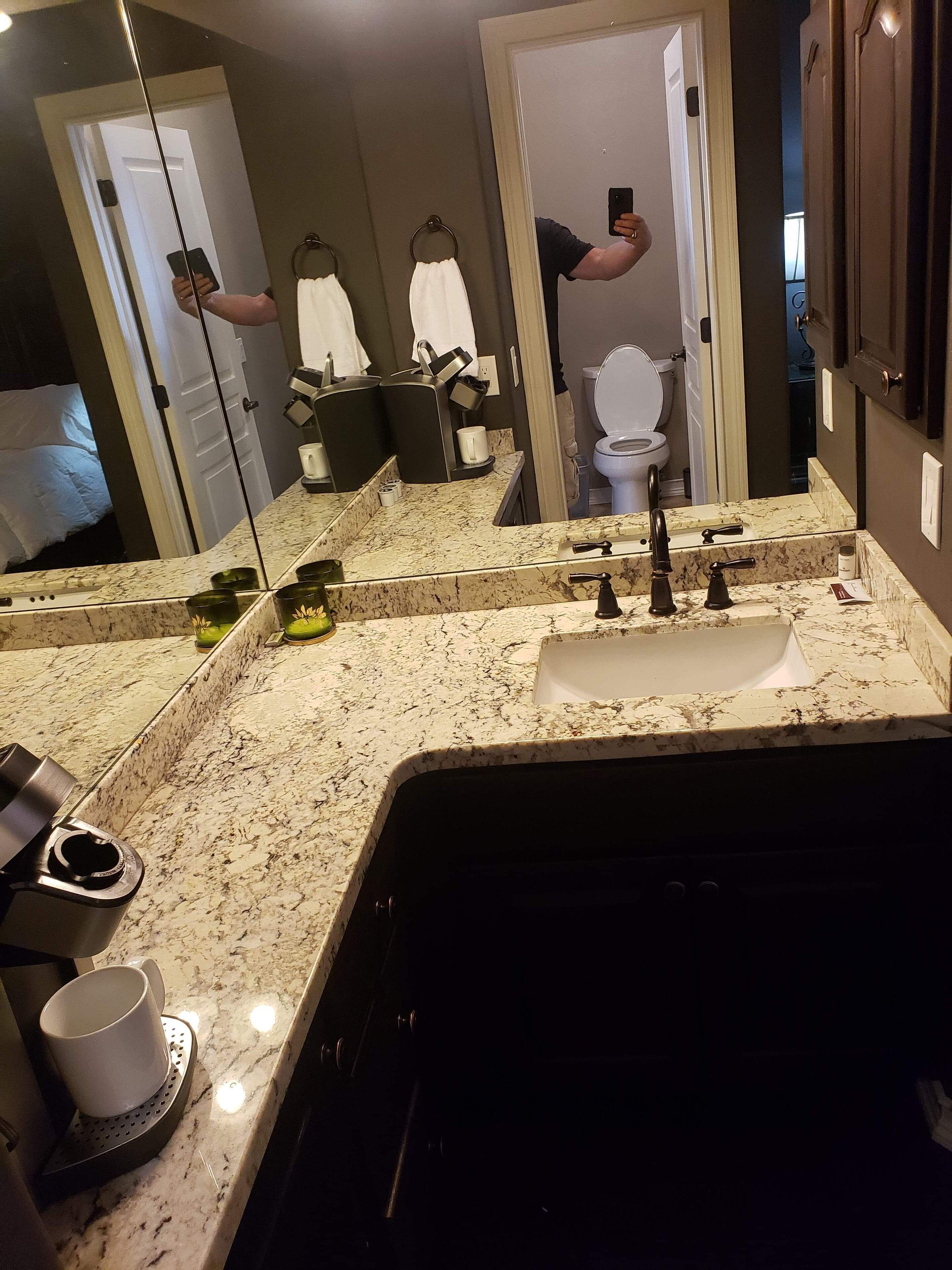 A bathroom with a large mirror, a sink with a marble countertop, a toilet, and a shower area.