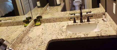A bathroom with a large mirror, a sink with a marble countertop, a toilet, and a shower area.