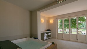 Een wellnessruimte met een groot bad, een plank met handdoeken en uitzicht op het landschap door grote glazen deuren.