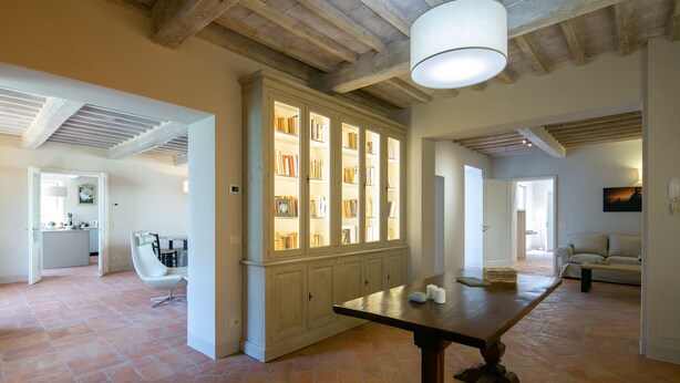 Een ruime kamer met een grote houten tafel, een inbouwkast en een moderne witte stoel.