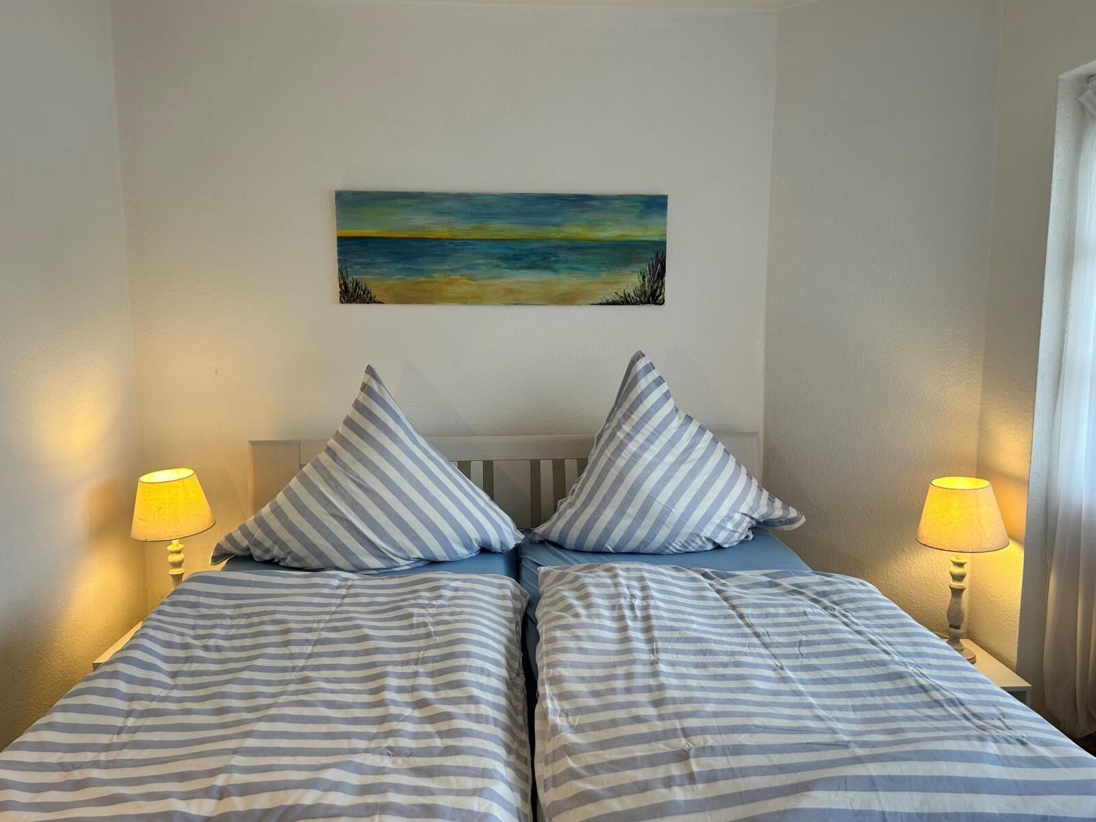 A double bed with striped bedding, two pillows, and two bedside lamps.