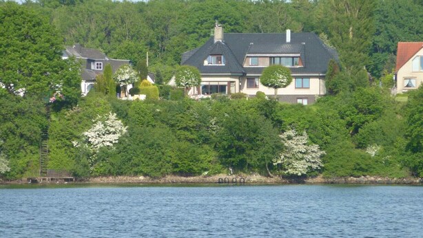 A large house with a dark roof, surrounded by dense greenery and a body of water. - "Seeschwalbe" Vacation Rental in Kappeln (Kappeln)